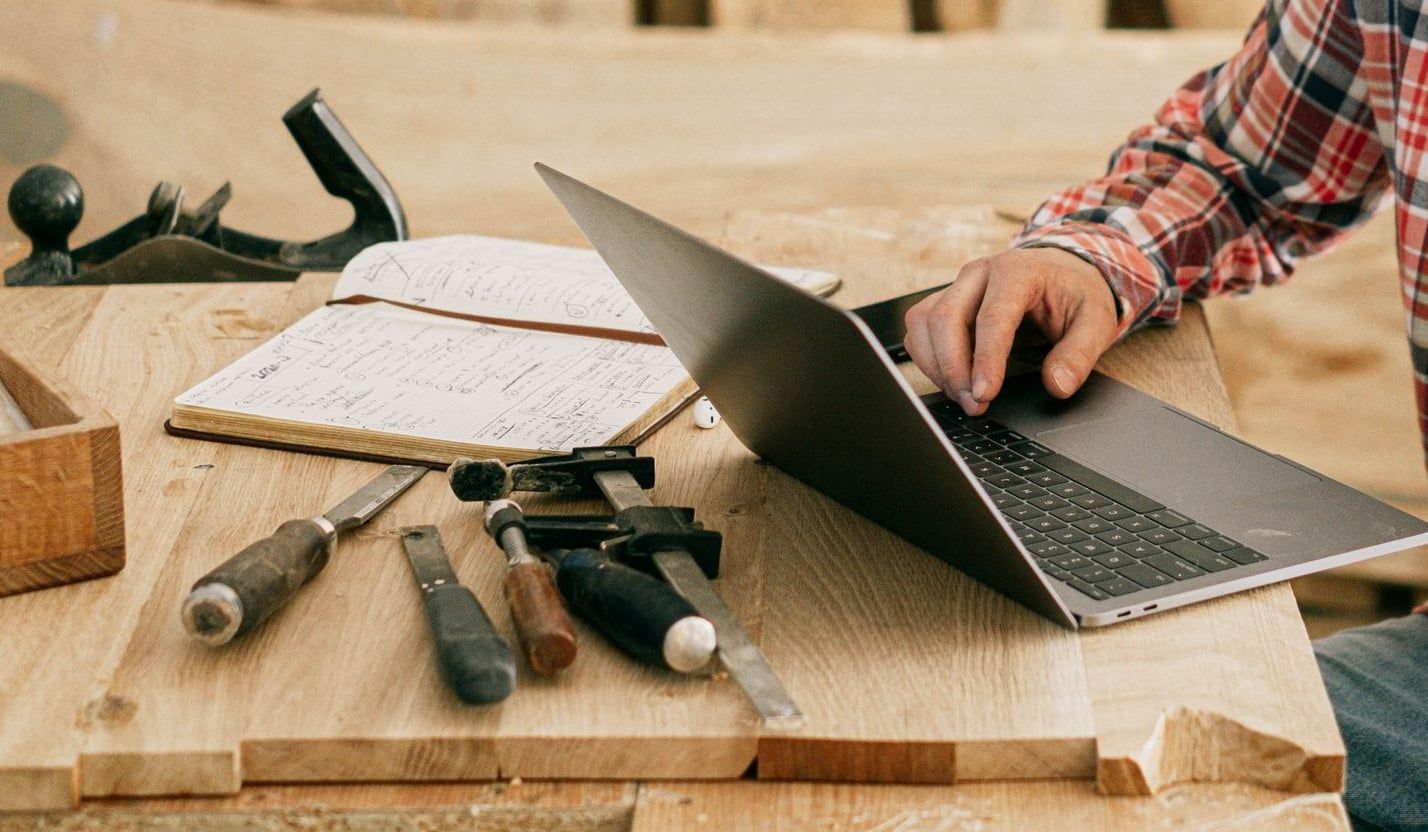 Un artisan travaille sur un ordinateur portable posé sur son établi, à côté de ses outils